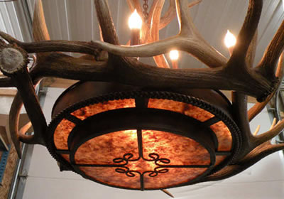 This chandelier provides a beautiful amber glow through the mica tiers while retaining a rustic elegance feel of an antler chandelier. Medium and small elk antler circle the center with tall patina coated copper sleeves for the 9 candles. This chandelier is custom built by the artist in Colorado USA.